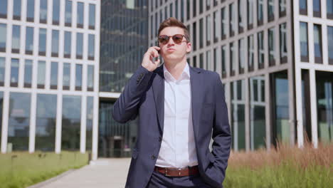 Young-man-in-suit-and-sunglasses-walks-and-talks-on-phone-outdoors