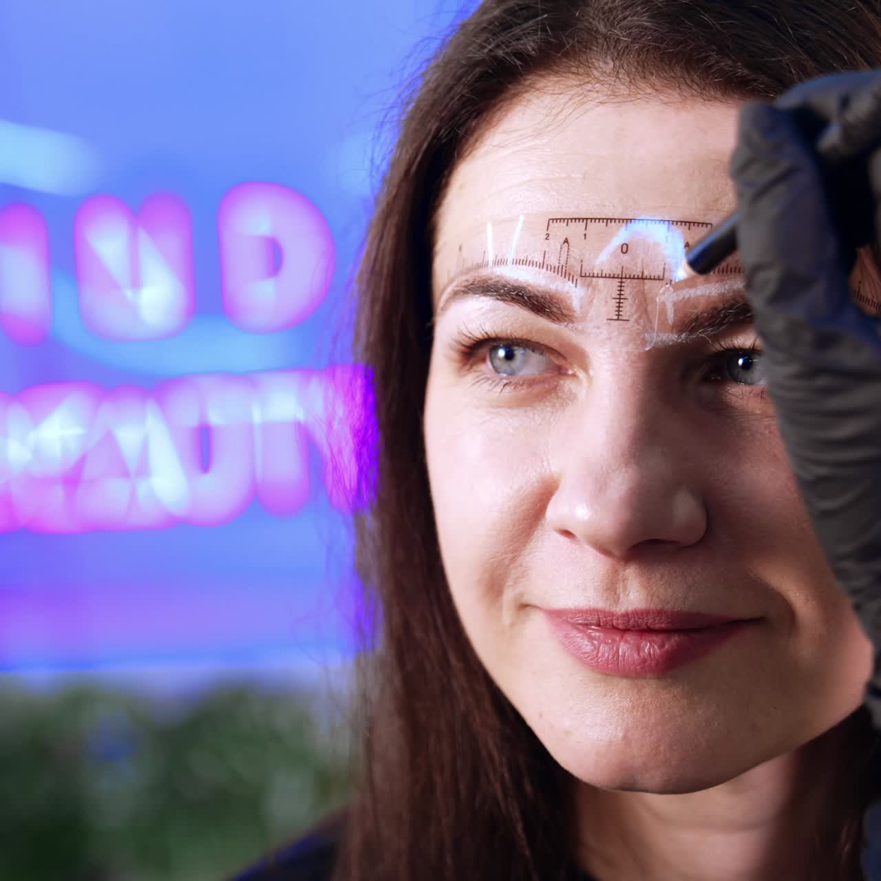 Special ruler is set on the female client's forehead. Beautician draws the lines with white pencil to mark the future eyebrow make up. Close up