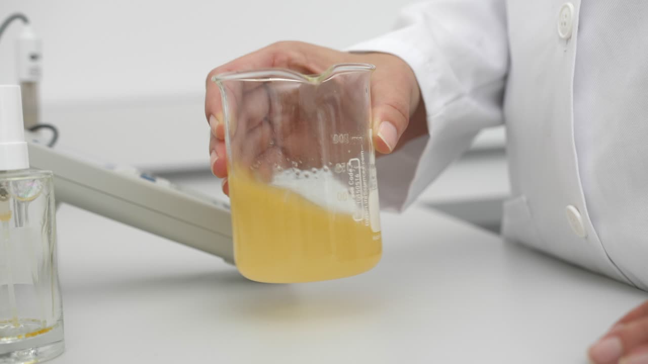 비이커에서 노란색 액체를 휘젓는 과학자의 세부 사항, 실내 자연 채광