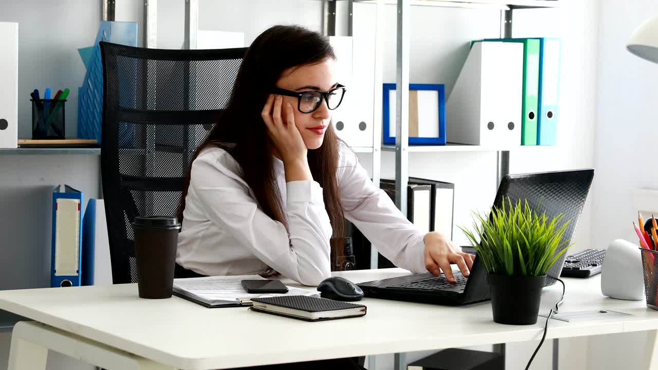 mujer apoyando la cabeza en la mano y usando la computadora portátil en la oficina moderna
