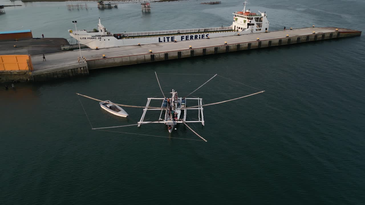 Aerial orbit of Taloot Argao Port, showcasing the docked boats and serene waters in Cebu, Philippines, during sunrise with intricate fishing vessel with multiple nets hanging off of double outrigger