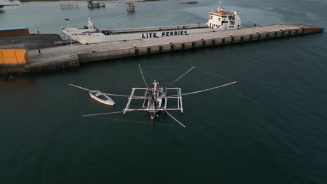 aerial orbit of taloot argao port, showcasing the docked boats and serene waters in cebu, philippines, during sunrise with intricate fishing vessel with multiple nets hanging off of double outrigger