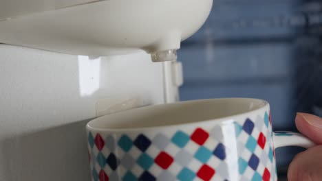 water poured from white plastic water dispenser tap into checkered pattern mug, close up