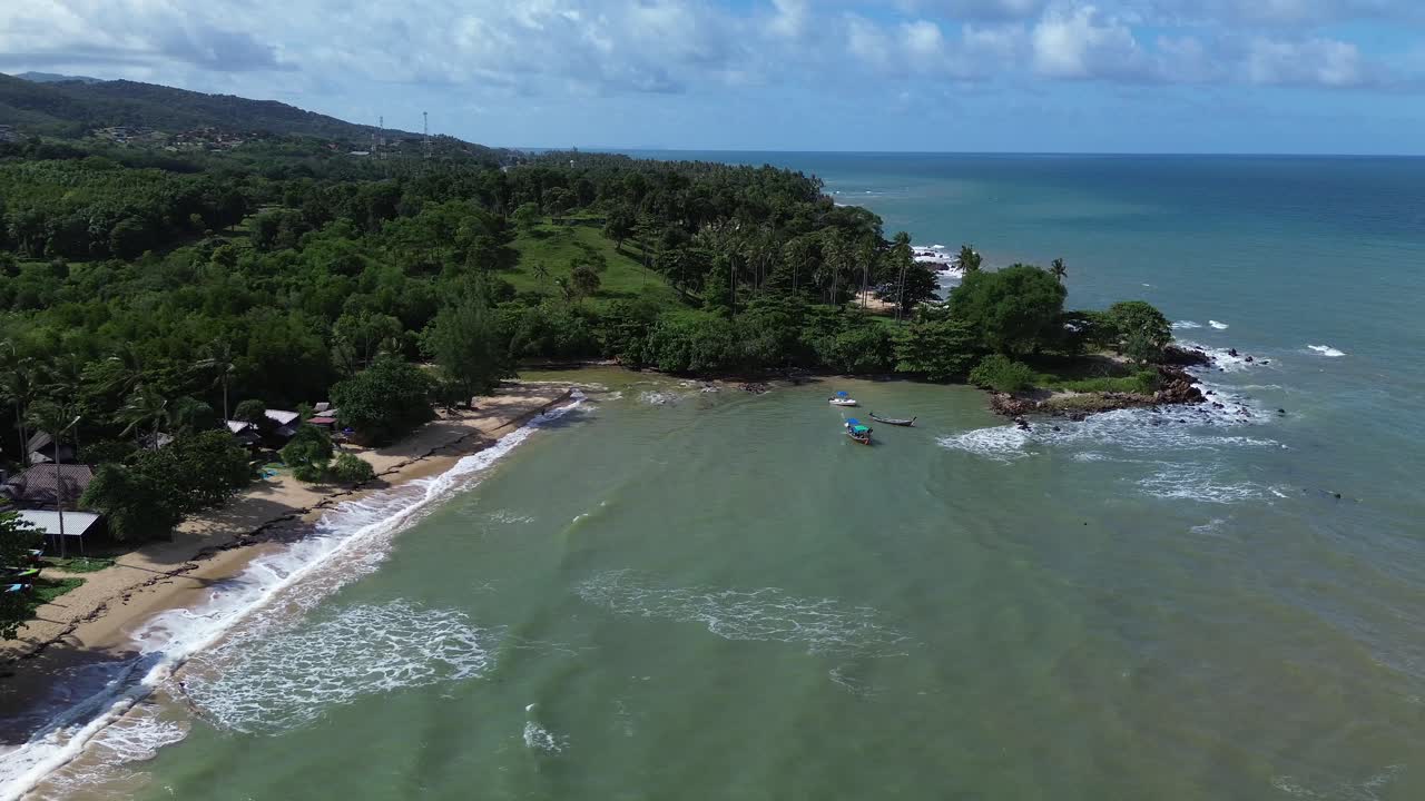 Aerial drone footage of Koh Lanta in Thailand showing longtail boats anchored by the shore, lush palm trees, tropical forest and rocky coastline with scenic turquoise sea