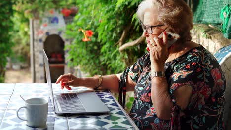 Ältere-Frau-Telefoniert-Am-Tisch-Mit-Laptop