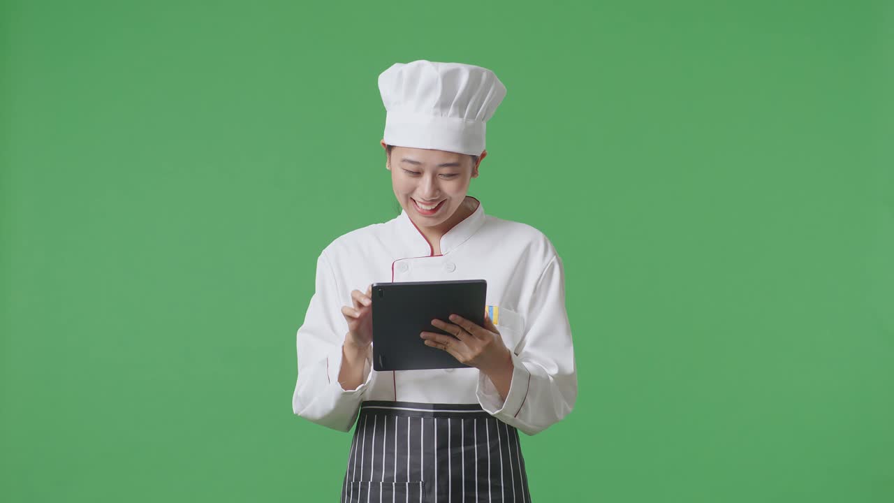 Asian Woman Chef Using A Tablet While Standing In The Green Screen Background Studio