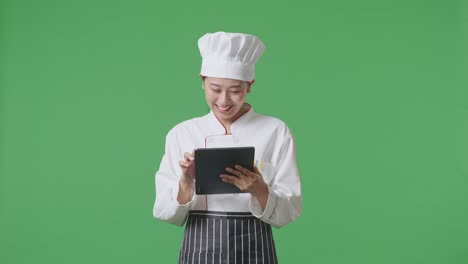 Asian Woman Chef Using A Tablet While Standing In The Green Screen Background Studio