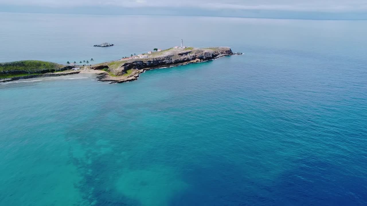 Isola dell'arcipelago di Abrolhos che emerge dalle acque turchesi dell'Atlantico, roccia frastagliata e macchie di vegetazione lussureggiante che incorniciano un incontaminato punto caldo marino celebrato per la conservazione e l'ecoturismo, ripresa con drone in avvicinamento