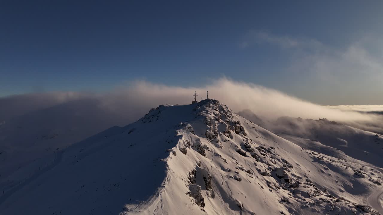 Cardrona mountain summit at sunrise, clouds flowing over snow-covered peak, New Zealand. Aerial drone panoramic view, copy space