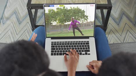 video de dos personas afroamericanas sentadas en el sofá y viendo un partido de fútbol en una computadora portátil