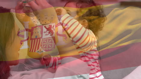 composite video of waving spain flag against caucasian mother playing with her baby at home