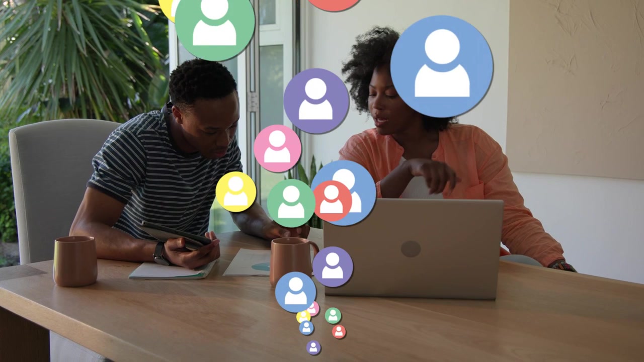 Couple reviewing laptop and paper at table, man tapping phone causing user icons expanding for tech
