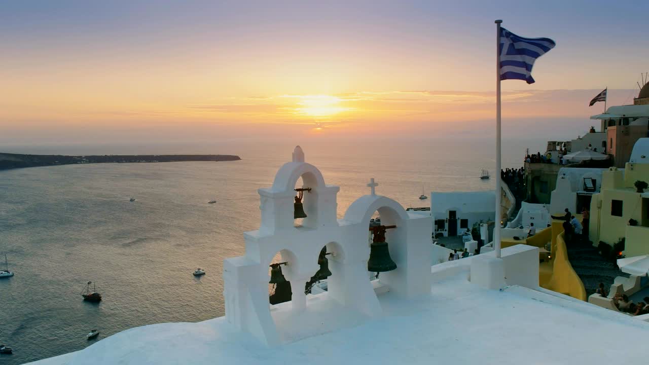 puesta de sol con bandera griega y campanas de la iglesia en oia, santorini