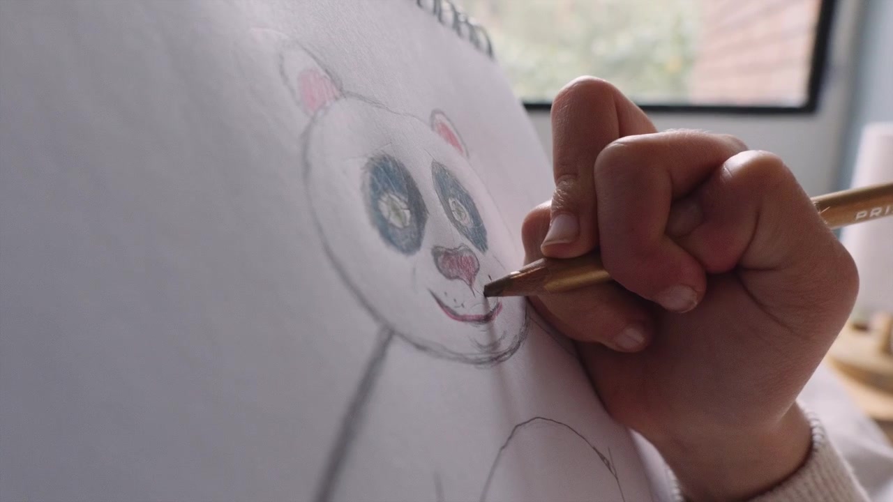 La mano de una niña pequeña dibujando un oso lindo en un trozo de papel.