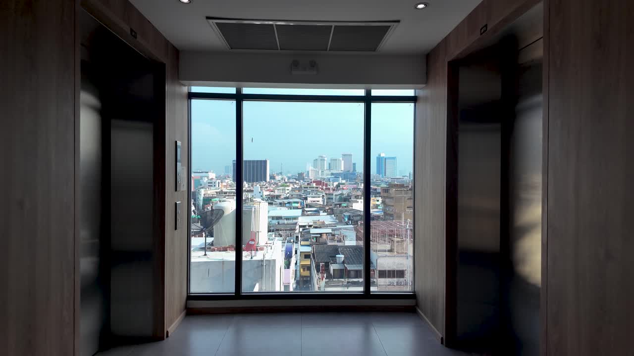 Building corridor with two elevators facing a window showing urban skyline buildings