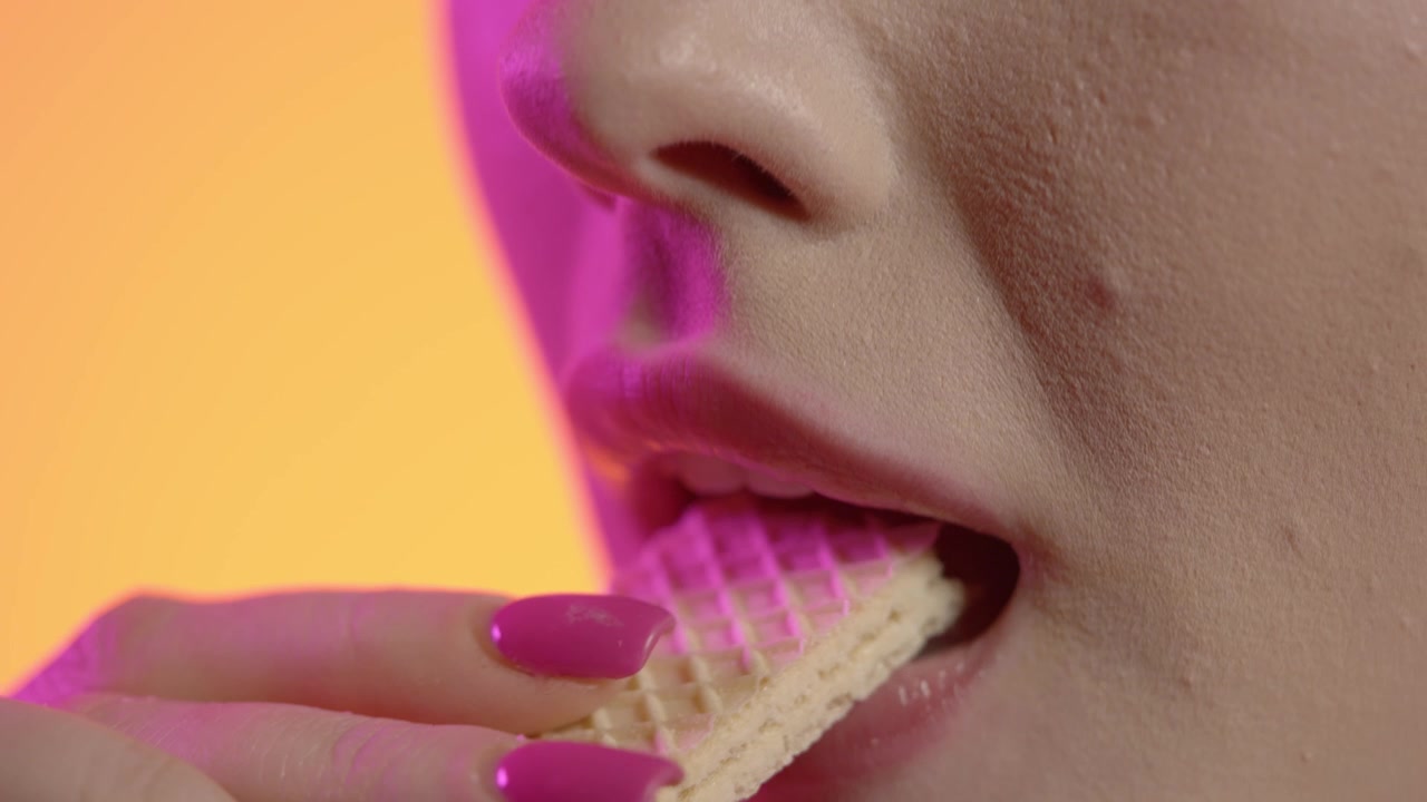 woman eating a crispy waffle in close-up, girly nail polish and red lipstick lips on green background