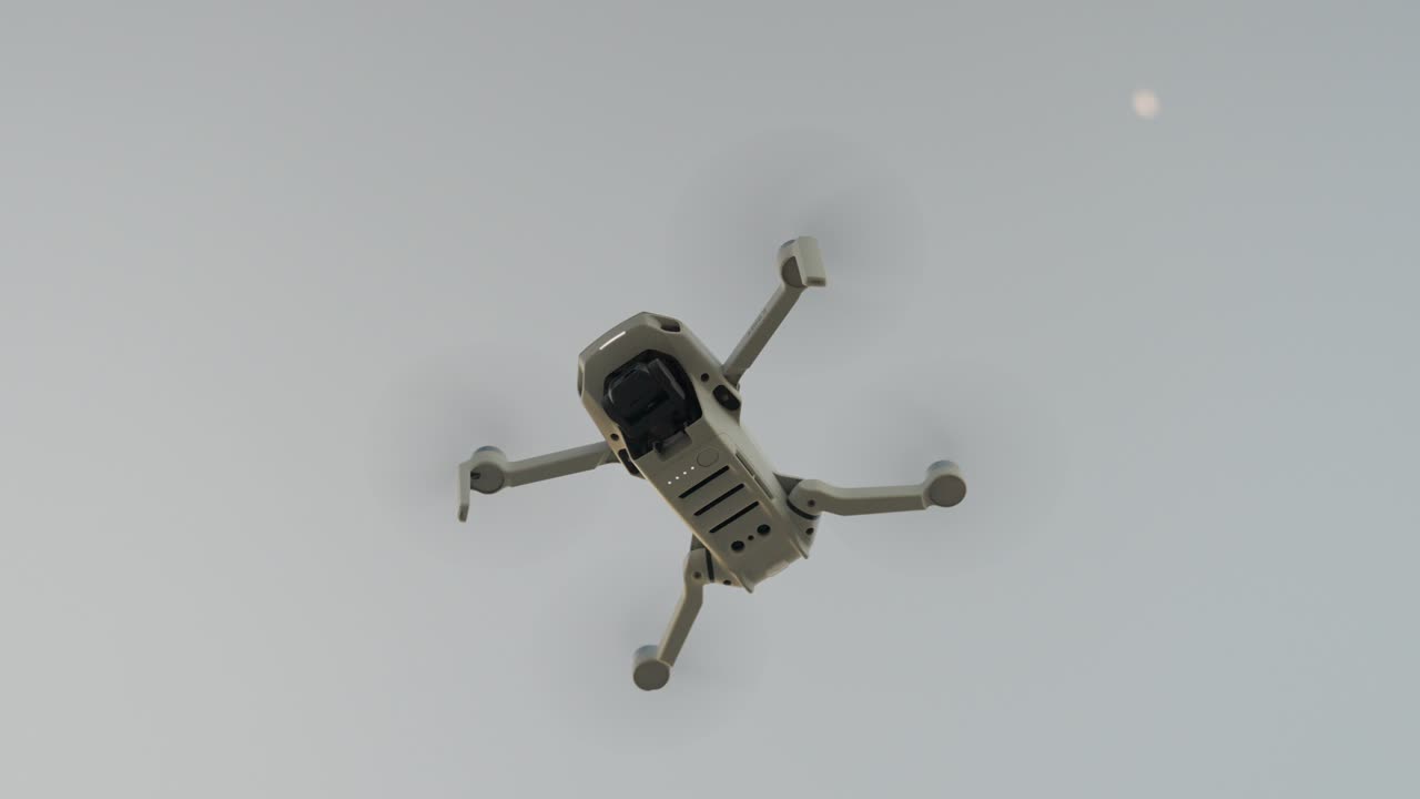 A white drone flying high in the sky during daytime with a distant moon in sight, aerial view