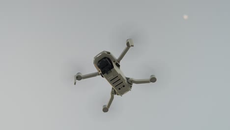 a white drone flying high in the sky during daytime with a distant moon in sight, aerial view