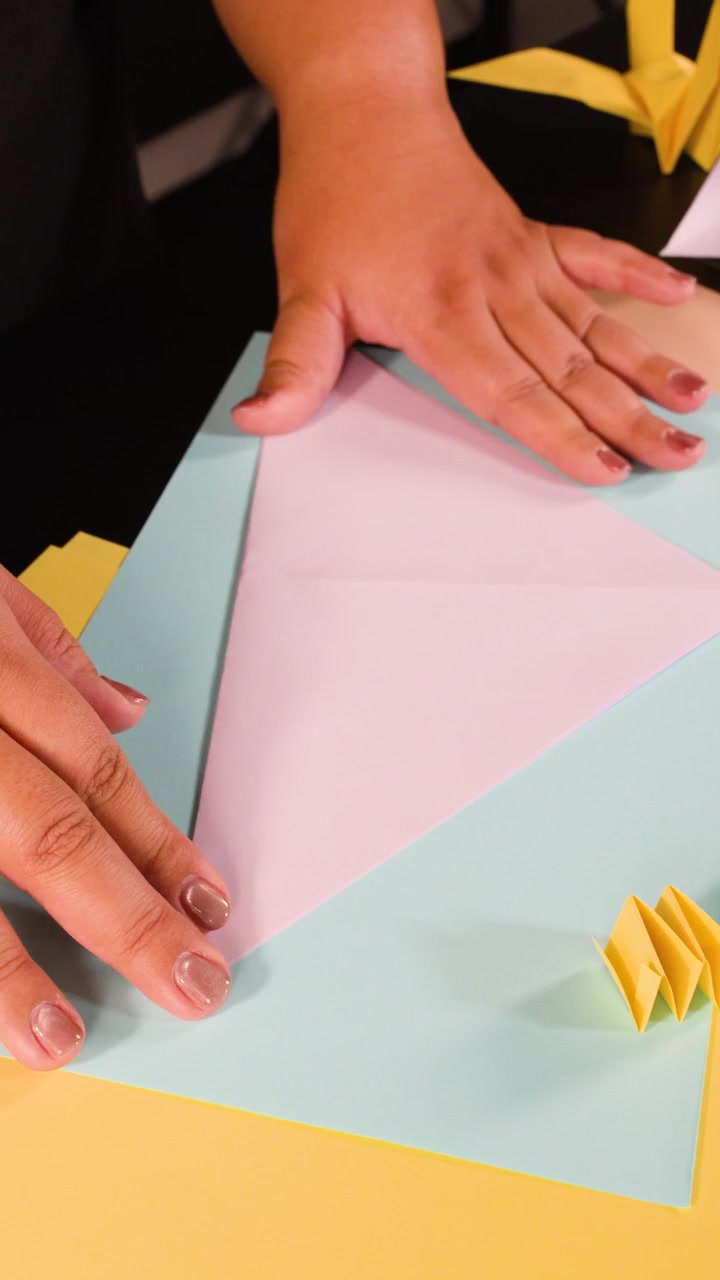 Nærbillede af hænder, der folder lilla papir til origami