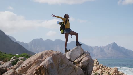 mujer afroamericana de pie en la roca con los brazos abiertos mientras trekking en las montañas