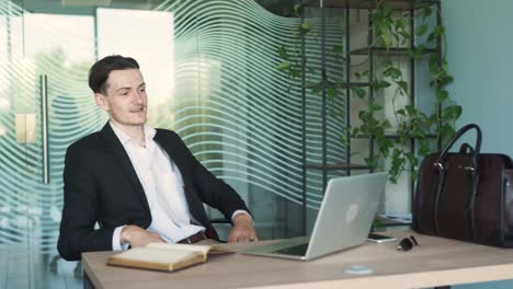 portrait of a handsome, young, stylish man in business attire sitting at a desk with a laptop in a modern office, looking disappointed by a loss