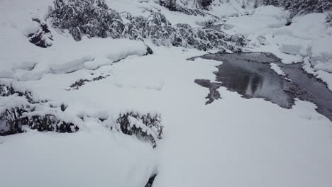 Drone-flying-over-a-creek-in-a-small-snowy-valley-in-the-alps