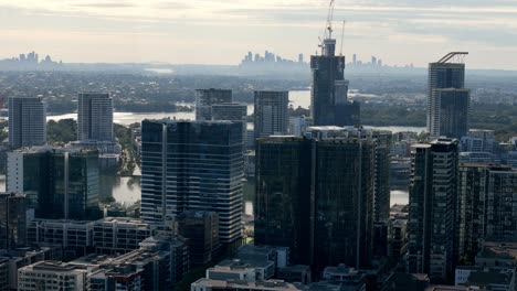 Stadterweiterung:-Glitzernde-Wolkenkratzer-Ragen-über-Dem-Fluss-Auf,-Mit-Entfernter-Stadtkulisse-Im-Morgenlicht