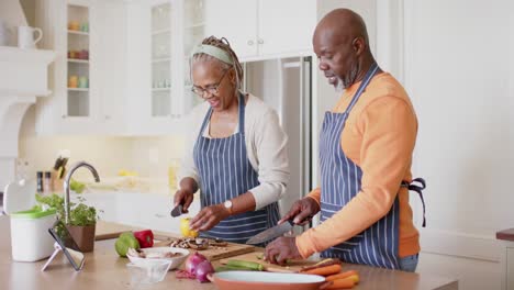 happy african american senior couple in aprons preparing meal in kitchen, slow motion
