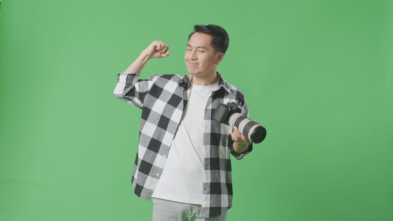 아시아 의 사진작가 는 스튜디오 의 녹색 스크린 배경 에 서 있는 동안 손 에 카메라 를 들고 팔꿈치 를 구부린다