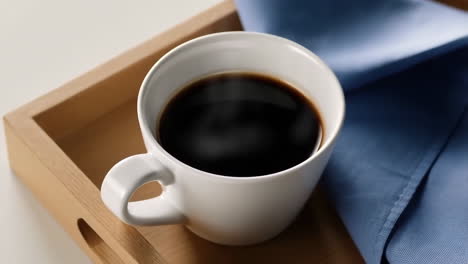 a cup of black coffee on a wooden tray