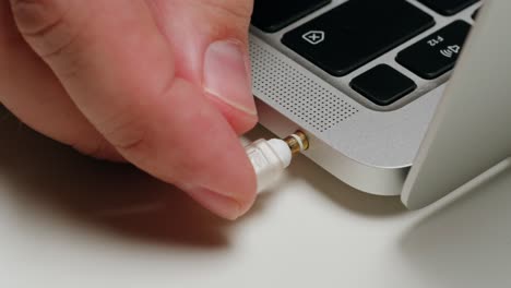 Hand plugging earbuds into laptop audio jack