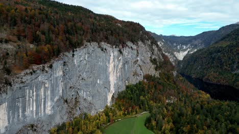 aerial view of a steep cliff face, with a winding river and a dense forest visible in the background