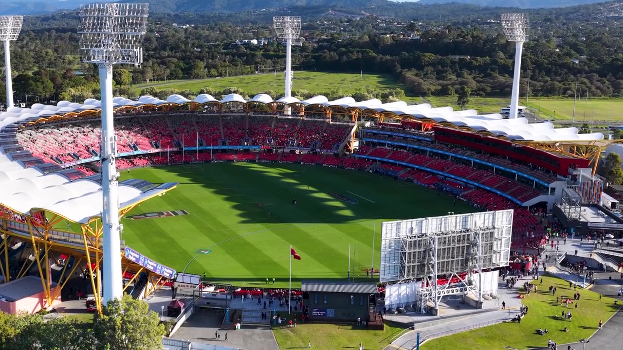 High angle drone shot of a large outdoor sports arena with green grass and seating.