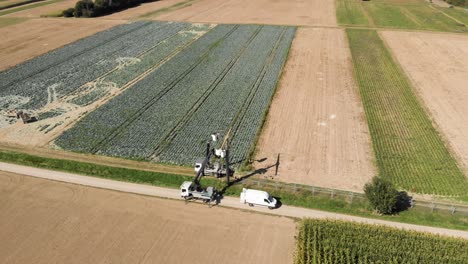 Aerial-shot-of-two-electricians-on-cranes-repairing-a-power-line-over-green-fields