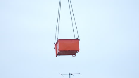 Medium-wide-shot-of-a-green-container-filled-with-roof-tiles-and-debris-getting-lifted-by-a-crane