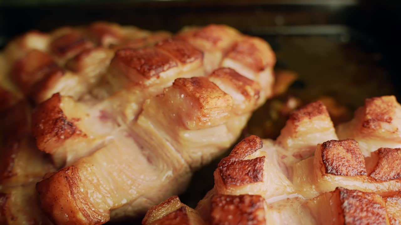 Primo piano di due tagli di maiale arrosto con cotenna croccante a griglia su una teglia, grasso sfrigolante e cotenna dorata e croccante, pronti da servire.
