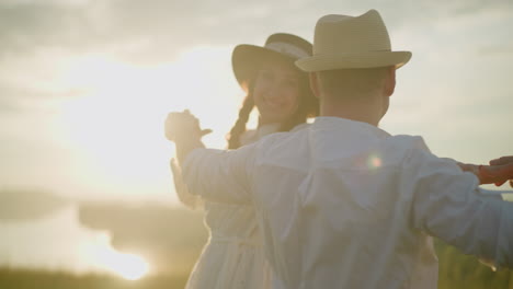 un primer plano de una pareja alegre bailando juntos al atardecer, ambos con camisas y sombreros blancos. la escena captura un tierno momento de felicidad y conexión, con la cálida luz del sol poniente