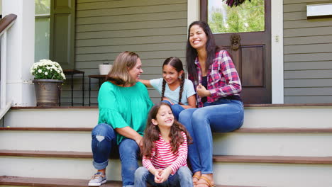 Familia-Femenina-De-Varias-Generaciones-Sentada-En-Los-Escalones-Frente-A-La-Casa