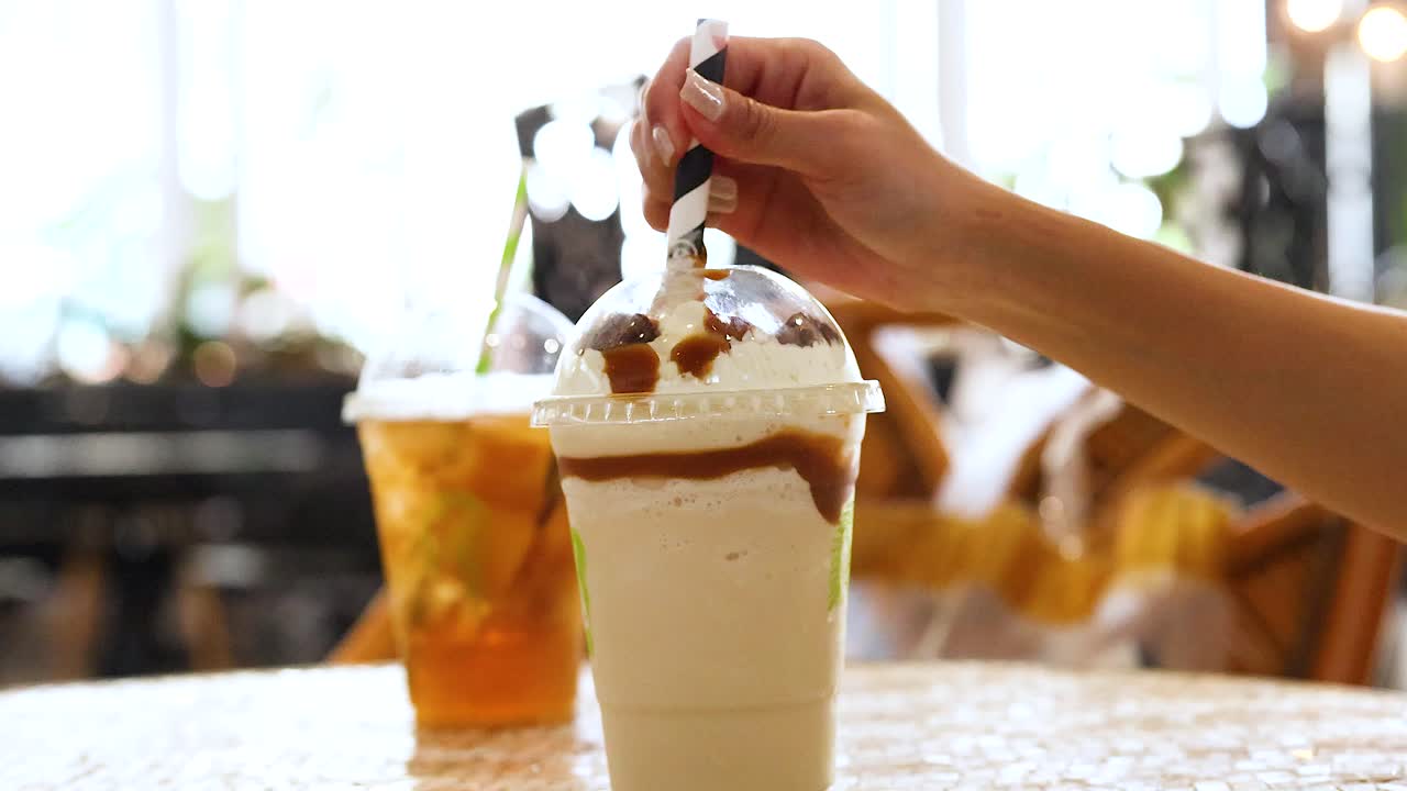 A hand stirs a creamy beverage with caramel topping, set against a sunlit cafe backdrop in Gold Coast, Australia