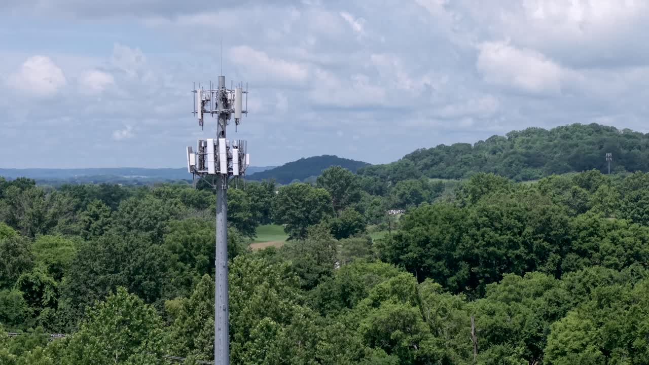 Cellular receiving and transmission tower microwave signal antenna antenna in a rural countryside with trees and meadows at daytime - ascending aerial reveal