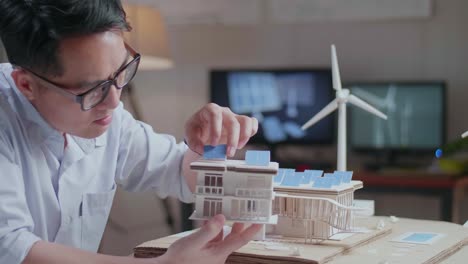 close up side view of asian man positively shaking her head while holding and looking at model of a small house with solar panel