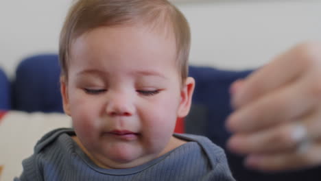 baby boy with boogers on his nose gets them wiped away by moms hands