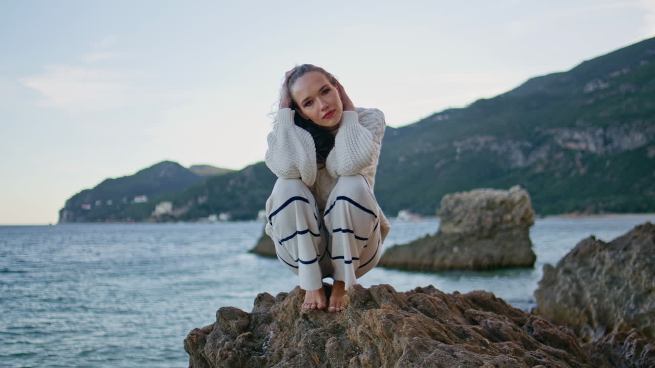 Woman sitting coastal rocks at calm evening. lady squatting on beach