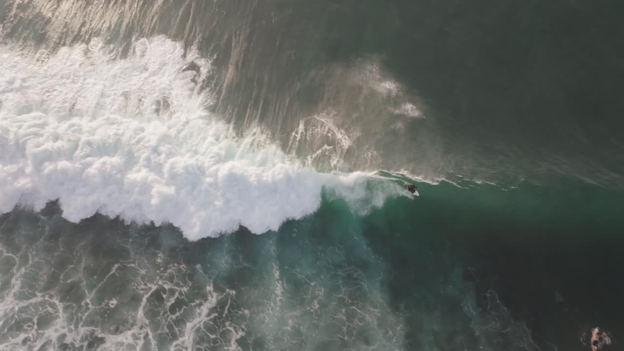 A 4k drone shot overhead a group of surfers chasing a wave in Bali where one surfer catches the wave