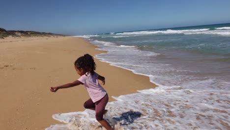 A-slow-motion-shot-of-a-young-girl-running-away-from-incoming-waves-on-a-beach