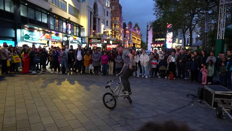 street performer on a bicycle entertains a crowd at night in london's vibrant leicester square
