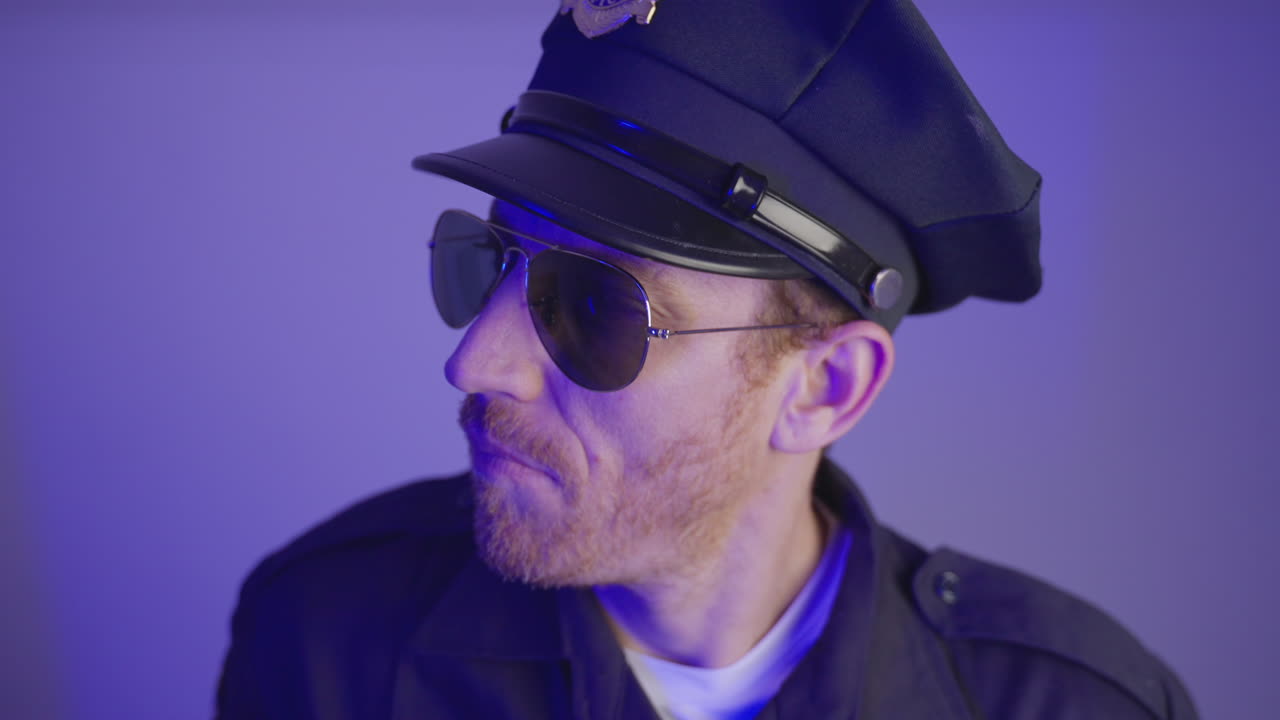 Funny cop or police officer with uniform is pretending to hold a gun. Gesture with hand as if carrying weapon. Wearing sunglasses making faces. Flashing red and blue lights with blank background