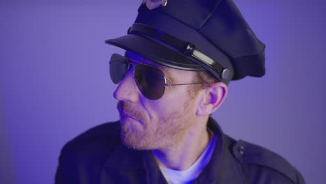 funny cop or police officer with uniform is pretending to hold a gun. gesture with hand as if carrying weapon. wearing sunglasses making faces. flashing red and blue lights with blank background