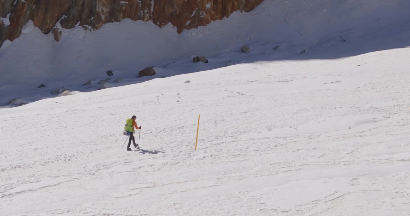 Everest region Nepal, aerial orbit shot circling a solo trekker walking through a completely snow-covered alpine trail surrounded by dramatic Himalayan winter scenery.