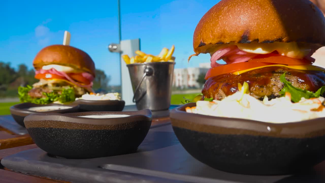 Close up view of two delicious gourmet cheeseburgers or hamburgers on a restaurant platter outdoors on a sunny terrace with french fries and mayonnaise visible in the bokeh foreground and background